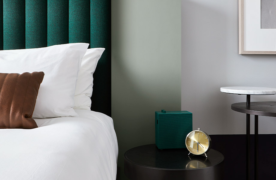 Habitación de hotel con ropa de cama blanca, cabecero verde oscuro, mesa de noche con reloj y pared decorativa en FENIX J0794 Verde Kitami